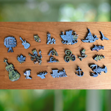 A set of small wooden puzzle pieces in various shapes, including a lighthouse, guitar, anchor, ship, and floral motifs, arranged on a wooden surface with a blurred green background.