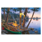 Canoe by a campfire on a lakeside with trees and a sunset.