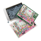 A completed jigsaw puzzle and its box are shown on a white background, with the open box revealing dark blue puzzle pieces. The puzzle features a colorful illustrated scene with a woman in a pink dress, a black cat.