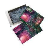 A completed jigsaw puzzle, its green box, and an open box filled with dark gray puzzle pieces are arranged on a white background. The puzzle features a colorful fantasy forest scene with glowing pink and green elements.