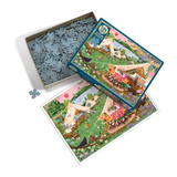 A jigsaw puzzle set shown on a white background, including the open box filled with blue-gray puzzle pieces, the puzzle box lid, and a completed puzzle featuring a whimsical outdoor scene with tents, campfires, and animals.