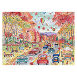 A completed jigsaw puzzle showing a colorful autumn village scene with trees in fall colors, cars, people, hot air balloons, and a market stall, displayed against a white background.