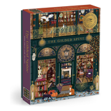 A boxed puzzle titled "The Gilded Spine" shown at a slight angle, revealing both the front illustration and the side panel. The box art depicts a detailed, ornate storefront with bookshelves, candles, lanterns, a fox, a cat, and decorative gold accents.