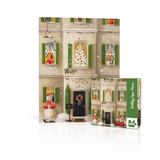 A 100-piece jigsaw puzzle titled 'Holiday Open Home' shown both flat-laid and in its green packaging box, featuring a festive Christmas village scene with a decorated house, snowman, and holiday decorations.