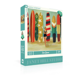 Jigsaw puzzle box featuring a woman and surfboards on a beach, with 'Janet Hill Studio' branding.