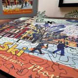 Jigsaw puzzle with a completed section of a winter scene, featuring people skiing and a tree.