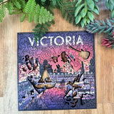 Jigsaw puzzle with 'Victoria' on a wooden surface with greenery