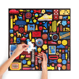 Colorful puzzle with various small objects and a hand placing a piece on a white background