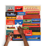 Person assembling a puzzle with colorful ship illustrations on a white background