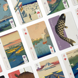 A close-up, angled view of a deck of illustrated playing cards arranged in a grid. The cards feature classic Japanese ukiyo-e style artwork, including landscapes, a large carp, a bridge, and mountain scenes, with suit symbols and card numbers visible.
