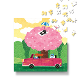 A colorful jigsaw puzzle featuring a whimsical scene of a pink convertible car driving under a giant pink flower tree with cartoon characters, shown with loose puzzle pieces floating above on a white background.