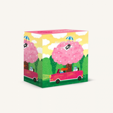 A square puzzle box with a whimsical illustration of pink trees, a pink car, and a yellow sky, photographed on a plain light background.