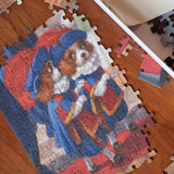 A completed jigsaw puzzle featuring two cartoon dogs dressed in red and blue clothing, placed on a wooden tabletop with a few loose puzzle pieces nearby.