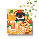 A completed jigsaw puzzle featuring a whimsical illustration of a black dog in a red beret sitting at a table with cakes, a pink candle, and green leaves, shown on a white background with a few loose puzzle pieces floating above.