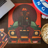 Puzzle box with a graphic design of a person sitting on a car, surrounded by a laptop, bowl of popcorn, and cards on a wooden table.