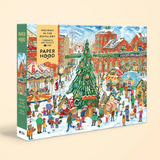 A 500-piece jigsaw puzzle box titled 'Holiday in the Distillery' by Paper Hood, featuring a colorful winter village scene with a Christmas tree, market stalls, and red brick buildings on a light beige background.
