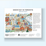 A 1000-piece jigsaw puzzle box for 'Snow Day in Toronto' by Paper Hood, featuring a colorful winter illustration of Toronto with snow, snowmobiles, and festive buildings, shown against a light blue background.