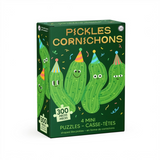 A boxed puzzle set labeled "PICKLES CORNICHONS" on a plain white background. The package is dark green with cartoon pickle illustrations in bright green, yellow, orange, blue, and pink, plus text reading "300 PIECES," "4 MINI PUZZLES," and "CASSE-TÉTES.