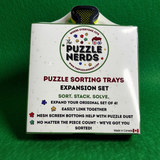 The Puzzle Nerds Puzzle Sorting Trays Expansion Set box on a green felt background. The white box features the brand logo and product details, with a black and yellow sorting tray visible at the top.