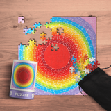 Colorful circular puzzle with missing pieces on a wooden surface, accompanied by a completed puzzle image and a black drawstring bag.