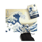 A completed and partially unpacked jigsaw puzzle featuring Hokusai's Great Wave off Kanagawa, shown with its matching cylindrical box and a black drawstring pouch on a white background.