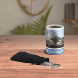 Puzzle canister with a black bag of puzzle pieces on a wooden surface