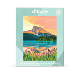 A rectangular jigsaw puzzle box shown against a plain white background. The front of the box features a colorful illustrated mountain lake landscape at sunset with a mountain peak, reflective water, dark tree lines, and purple flowers in the foreground.