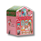 A 100-piece Christmas-themed biscuit shop puzzle in a house-shaped box. The packaging features a pink brick facade, a red and white 'BISCUITERIE' sign, and colorful holiday illustrations of Santa Claus, cookies, candy canes, and snowman on a white background.