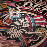 A close-up of a circular jigsaw puzzle featuring a colorful tattoo-style skeleton wearing a pink and white striped top hat on a black background.