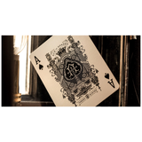 An Ace of Spades playing card from the Old Spades deck, featuring an ornate black crest design on an aged cream background, shown at an angle against a dark, moody background.