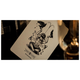 A close-up of a playing card featuring The Joker illustration, with the text 'THE JOKER' and 'HUDSON' visible, photographed in warm, moody lighting with dark background elements and a blurred glass on the right.