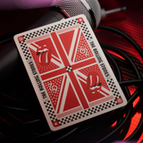 A playing card featuring a red and white Union Jack-style design with the Rolling Stones logo and text, photographed on top of a microphone and coiled cables under red lighting.