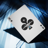 A single playing card shown at an angle on a dark blue metallic surface. The card is white with black suit symbols and a central black-and-white spaceship graphic with a small blue accent.
