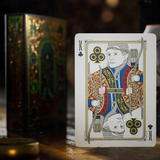 A single playing card, King of Clubs, stands upright on a reflective wooden surface. The card features an ornate illustration of a warrior in traditional Tolkien goblin attire with red, gold, and blue details.