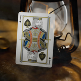 A King of Spades playing card is displayed upright, leaning against a vintage-style lantern on a rustic wooden surface.