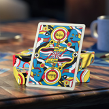 A colorful illustrated deck of playing cards stands upright on stacked matching card boxes on a wooden table. The card art features stylized blue figures, a Union Jack, and circular logos reading 'The Beatles' and 'smile'.